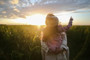 A father holding daughter in a field at sunset as she points upward, reflecting time together after Houston custody case.