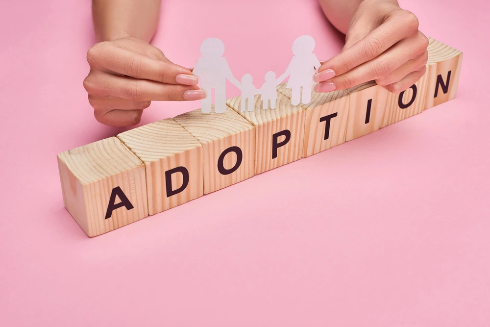 hands holding a paper cut out family with the word adoption on blocks