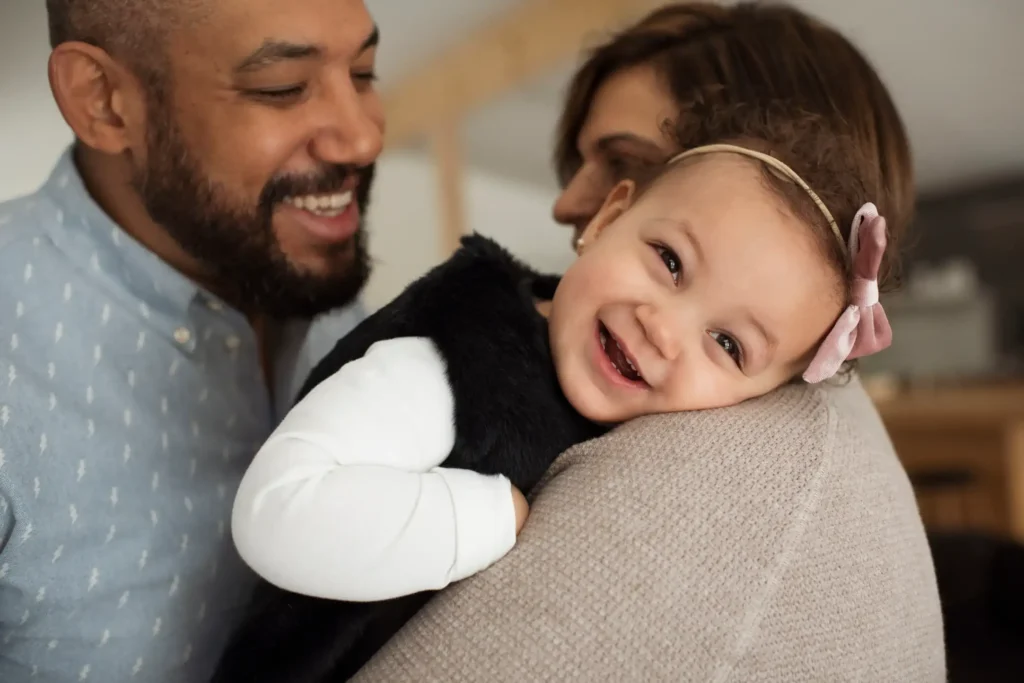 Smiling toddler held by a parent, with both adults looking on lovingly—symbolizing a joyful moment in a newly formed adoptive family.