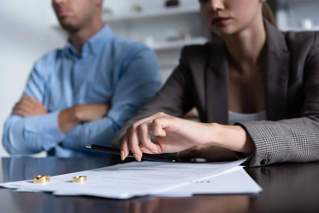 Close-up of a couple seated at a table with divorce papers and wedding rings, suggesting a contested divorce discussion in progress.